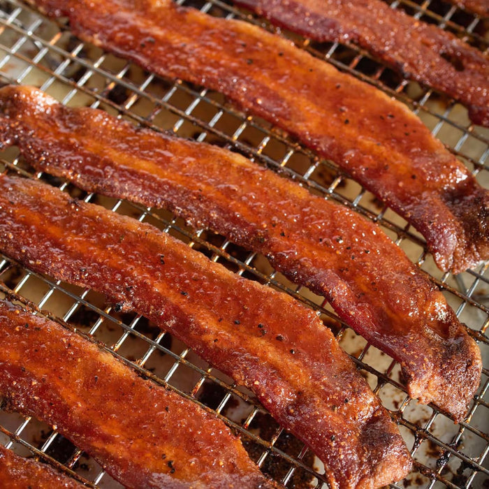 Strips of thick cut bacon are coated in a sweet and savory glaze and baked to a crisp finish on a wire cooling rack.