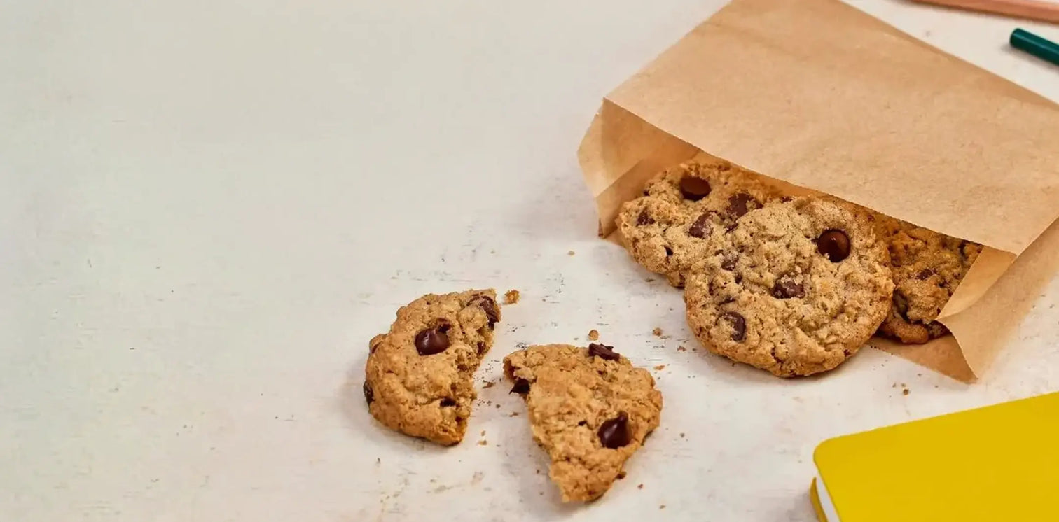 Cookies spilling out of a brown paper bag on a light surface with a yellow object in the corner.