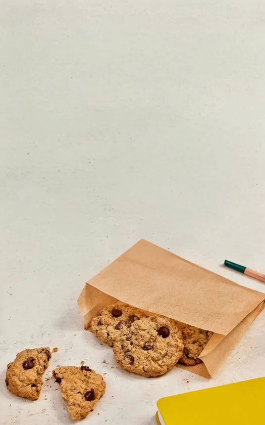 Open brown paper bag of cookies with a few cookies spilled out on a light surface.
