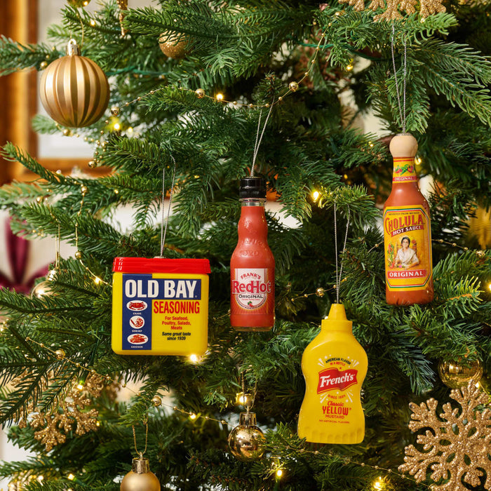 A festive Christmas tree is decorated with ornaments shaped like bottles of Cholula Hot Sauce, Frank's RedHot, French's Mustard, and a tin of Old Bay Seasoning.