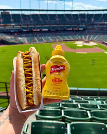 a hot dog with french's classic yellow mustard with a background of a baseball field on opening day