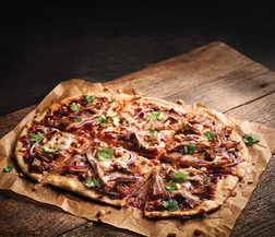 A freshly baked pizza topped with shredded meat, melted cheese, red onion, and cilantro, served on parchment paper over a rustic wooden board against a dark background.