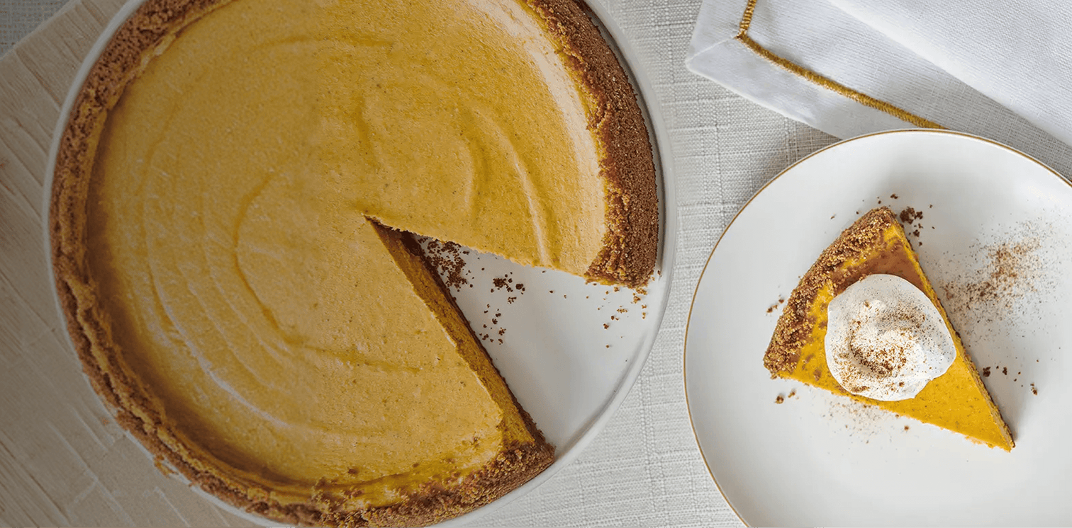 Pumpkin pie with a slice removed, served on a white plate with a decorative rim.