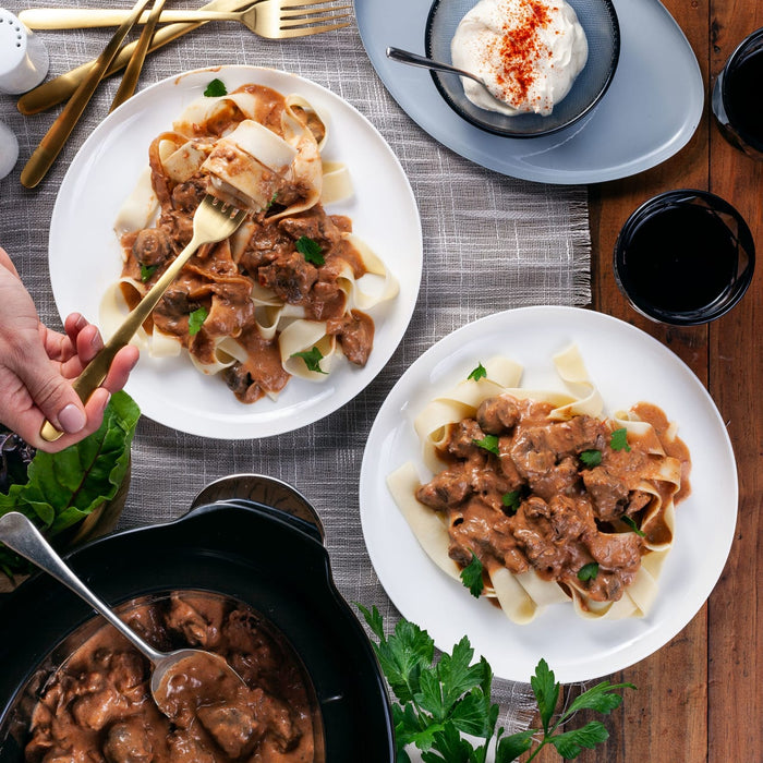 ['A plate of beef stroganoff with noodles and a side of sour cream.']