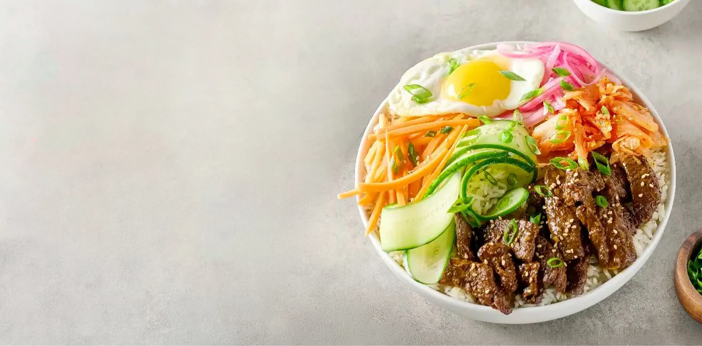 Bowl of Korean-style beef bibimbap with various ingredients on a light gray background