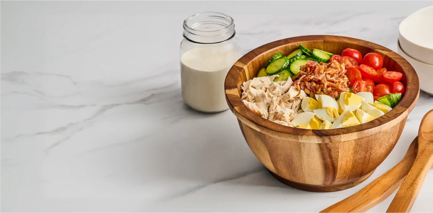 Wooden bowl with salad on a marble surface next to a jar of dressing.