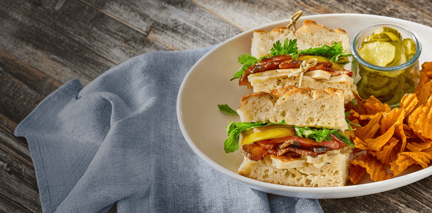 Sandwich with chips and pickles on a plate with a wooden background