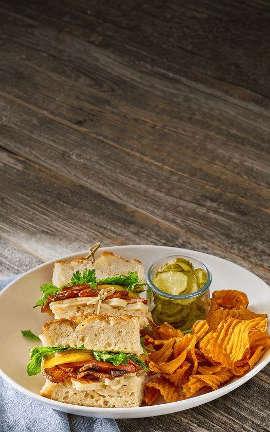 Sandwich, chips, and pickles on a plate with a wooden background