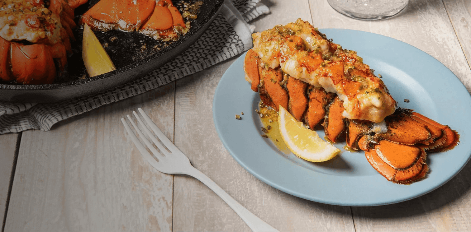Lobster tail on a blue plate with lemon wedges on a wooden table.