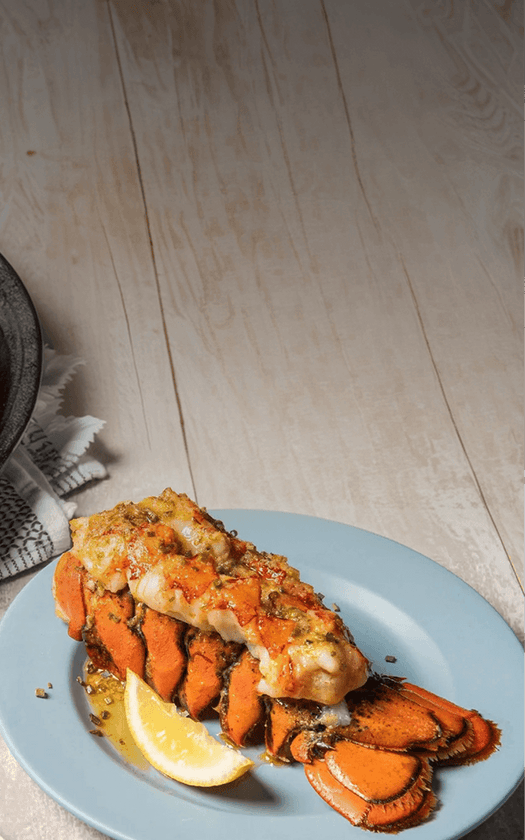 lobster tail on a blue plate with a lemon wedge on a wooden surface