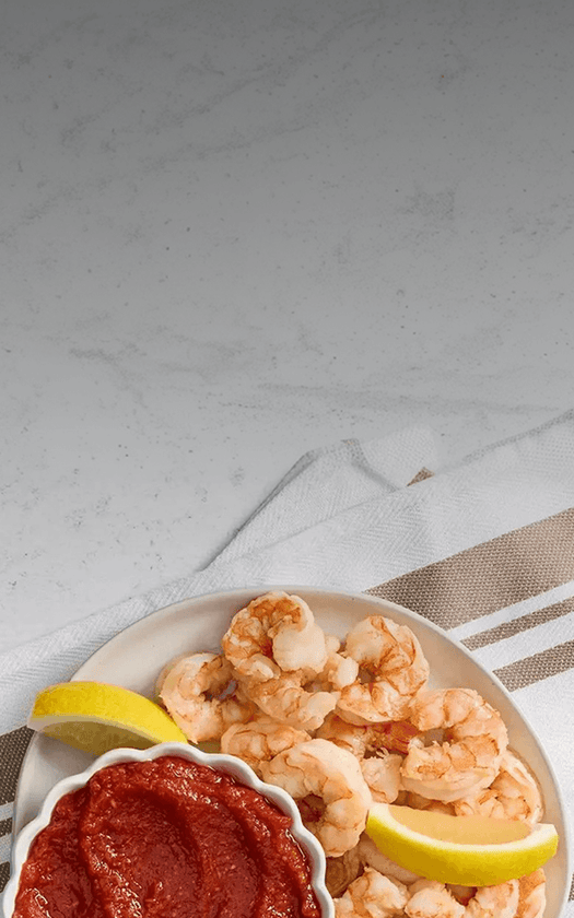 Shrimp with lemon wedges and a red sauce on a white plate against a light gray background.