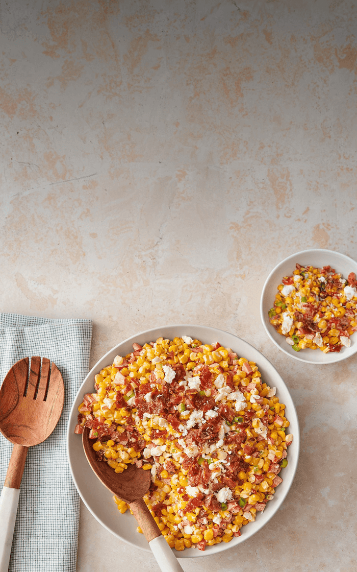 Corn salad with bacon and cheese in a white bowl on a beige surface
