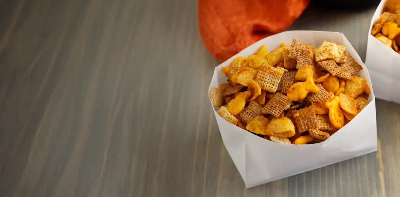 Two paper bags filled with a mix of cereal and snack bars on a wooden surface.