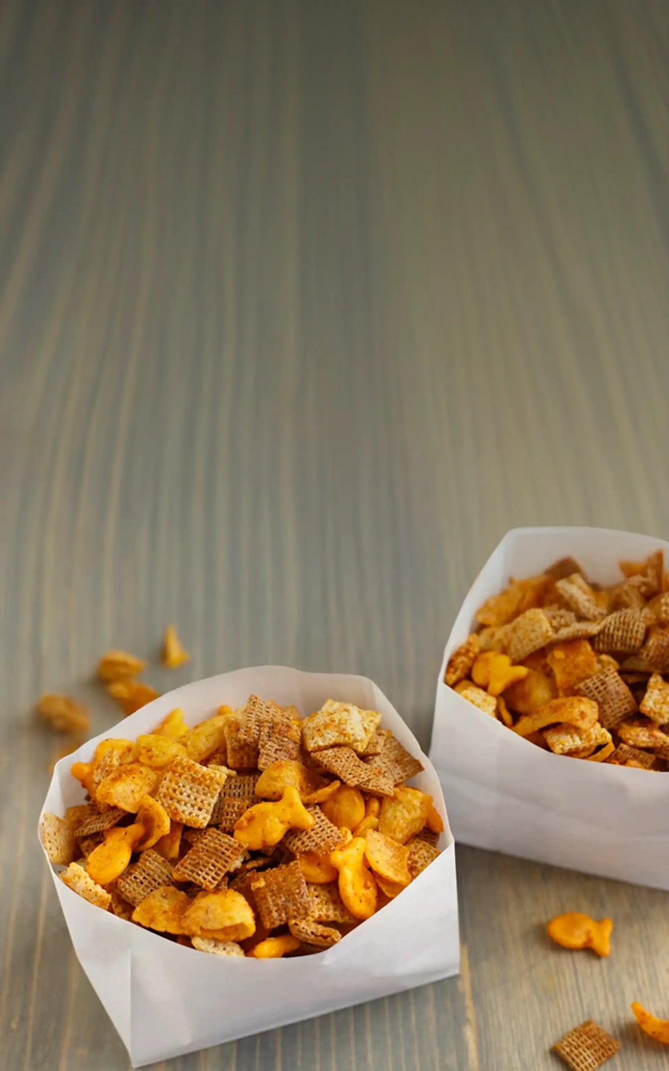 Two paper bags filled with a mix of cereal and snack bars on a wooden surface.