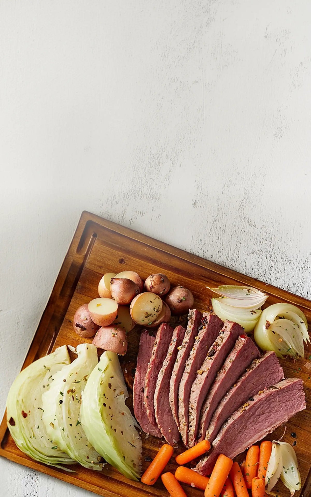 Wooden cutting board with sliced corned beef, carrots, and onions on a light gray background