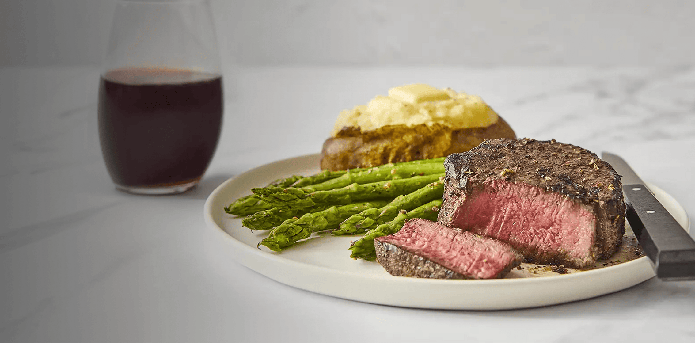 Steak, asparagus, and mashed potatoes on a plate with a glass of red wine.
