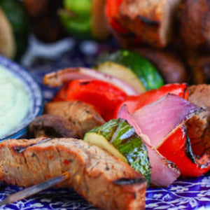A close-up of a skewer with grilled meat, vegetables, and onions.