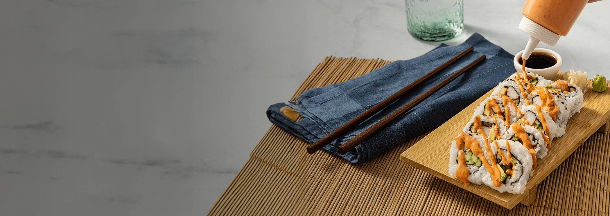 Sushi rolls with orange sauce on a wooden board with chopsticks and a denim napkin.