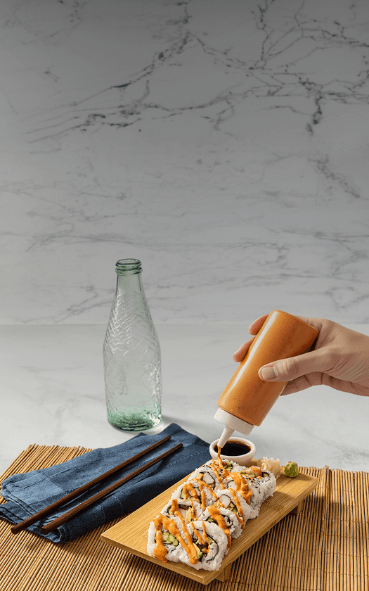 Person pouring sauce over sushi on a marble countertop