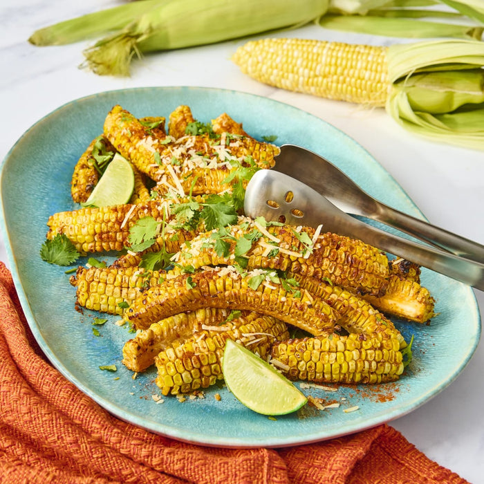 A platter of grilled corn on the cob, garnished with lime wedges, cilantro, and shredded cheese, is ready to be served.