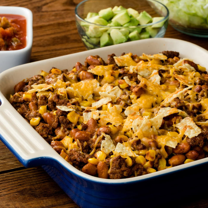 A casserole dish filled with a cheesy beef and corn casserole topped with tortilla chips.
