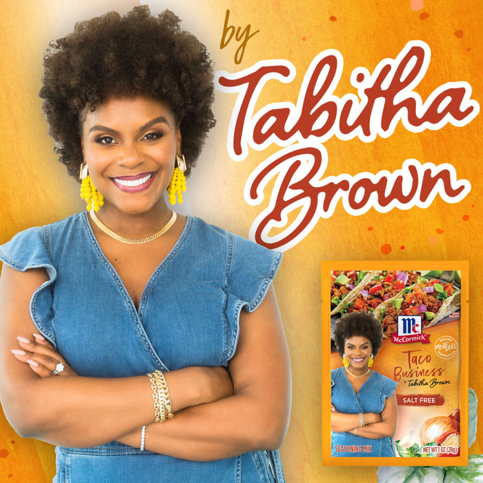 Tabitha Brown smiles while holding a McCormick Taco Business seasoning packet.