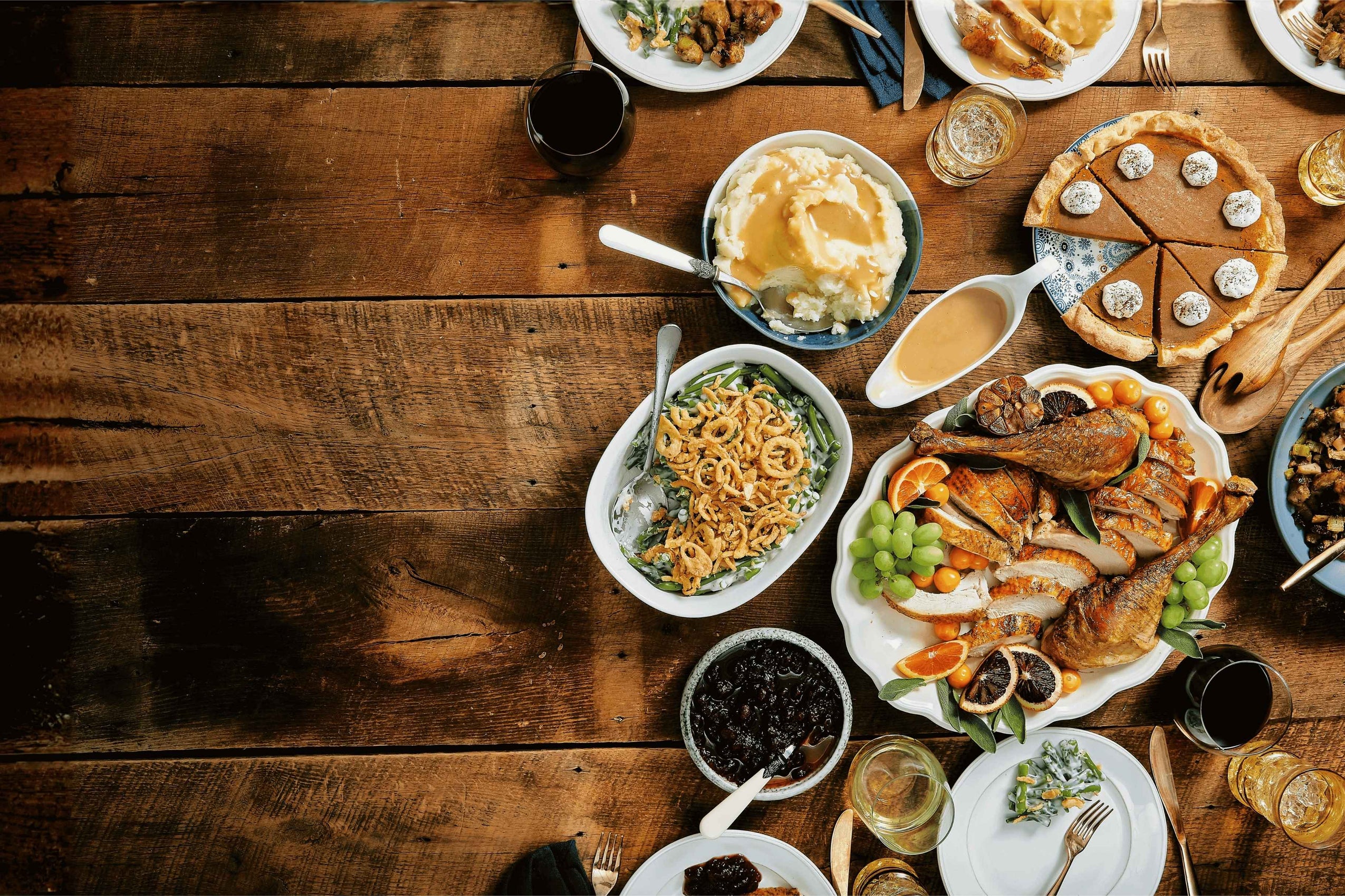 Diverse array of food on a wooden table with various dishes including a pie, pasta, and meats.