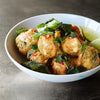 A white bowl filled with golden fried fritters seasoned with Mccormick Culinary Turmeric Spice Ground 16 Oz and topped with a creamy orange sauce, fresh cilantro, and sliced red chilies.
