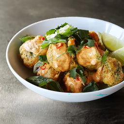 A white bowl filled with golden fried fritters seasoned with Mccormick Culinary Turmeric Spice Ground 16 Oz and topped with a creamy orange sauce, fresh cilantro, and sliced red chilies.