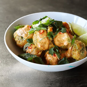 A white bowl filled with golden fried fritters seasoned with Mccormick Culinary Turmeric Spice Ground 16 Oz and topped with a creamy orange sauce, fresh cilantro, and sliced red chilies.