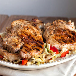 Grilled pork chops with cabbage and red peppers on a white plate.