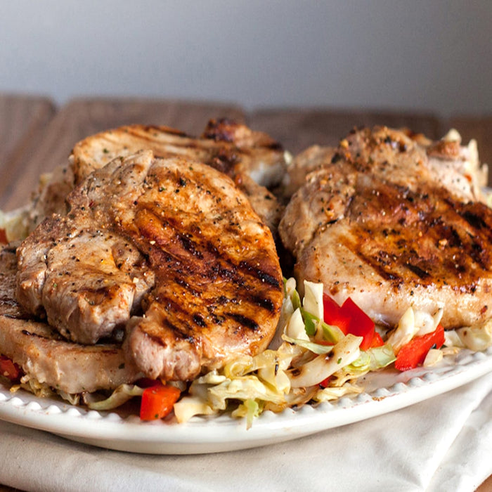 Grilled pork chops with cabbage and red peppers on a white plate.