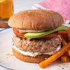 A close-up of a turkey burger with avocado, tomato, and a side of sweet potato fries.