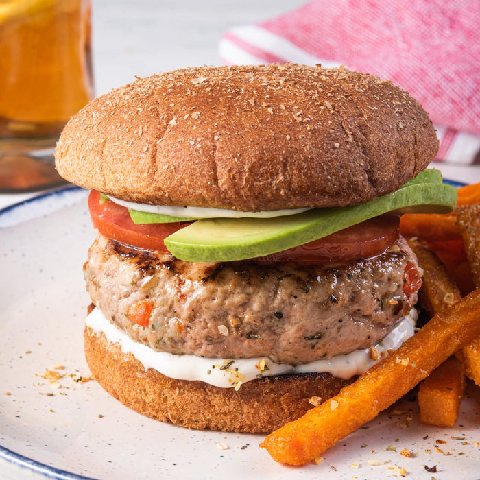 A close-up of a turkey burger with avocado, tomato, and a side of sweet potato fries.