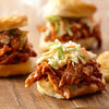 Three pulled pork sliders with coleslaw on a wooden board.
