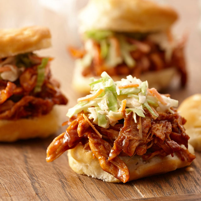 Three pulled pork sliders with coleslaw on a wooden board.