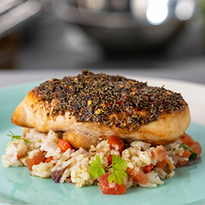 A close-up of a chicken breast with a crispy crust served over a bed of rice with tomatoes and herbs.