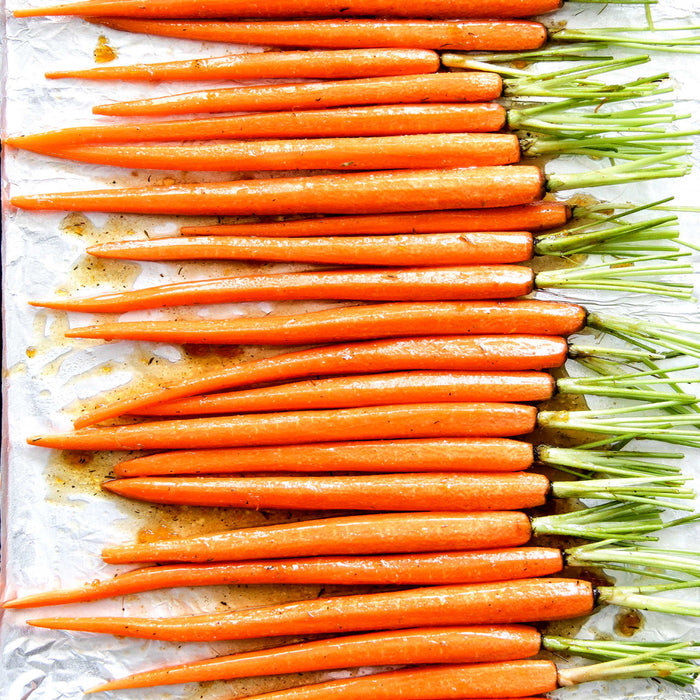 A close-up of a baking sheet with a row of roasted carrots.