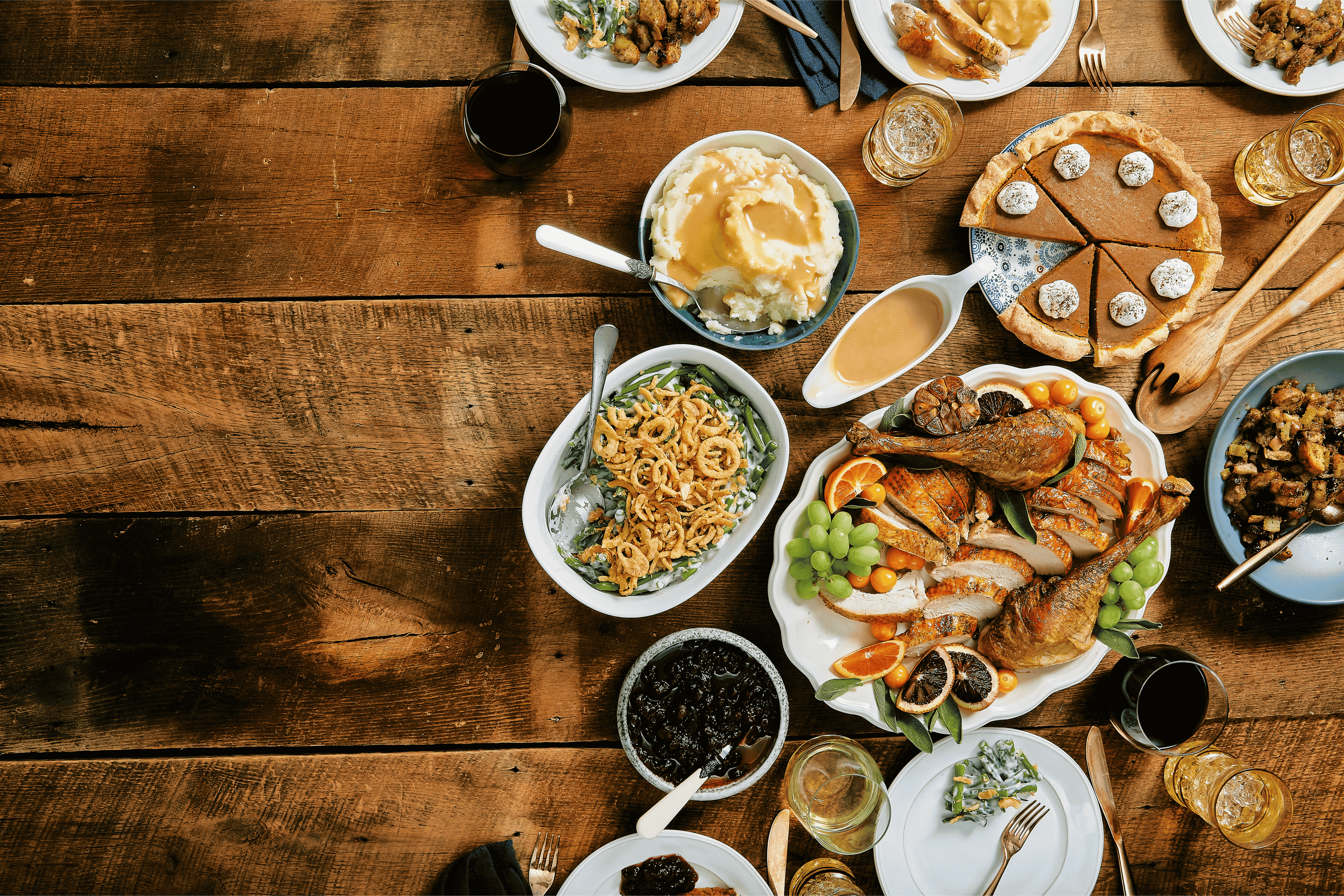 Diverse food spread on a wooden table with various dishes including a pie, salad, and meats.