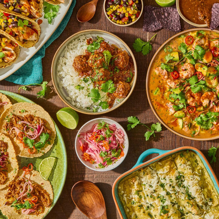 A festive spread of Mexican cuisine featuring tacos, enchiladas, and a shrimp dish, with a bottle of Cholula Green Sauce 12 Fl Oz prominently displayed among other condiments.