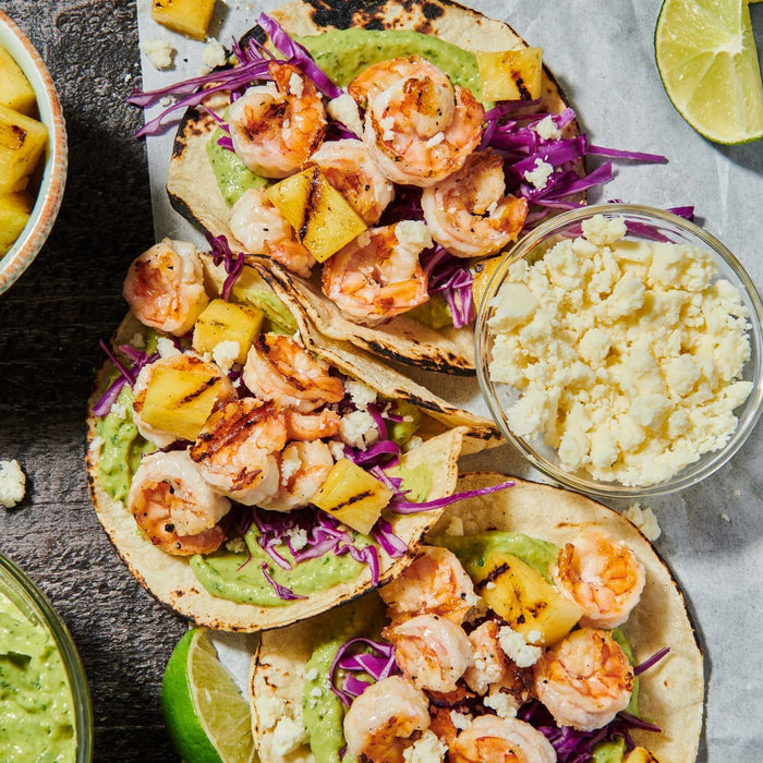 A vibrant close-up of shrimp tacos with grilled pineapple, red cabbage slaw, and avocado crema, showcasing a fresh and flavorful meal.
