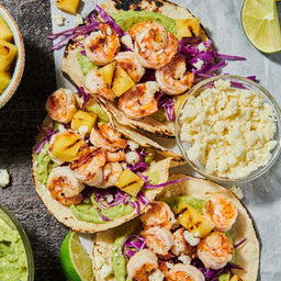 A vibrant close-up of shrimp tacos with grilled pineapple, red cabbage slaw, and avocado crema, showcasing a fresh and flavorful meal.
