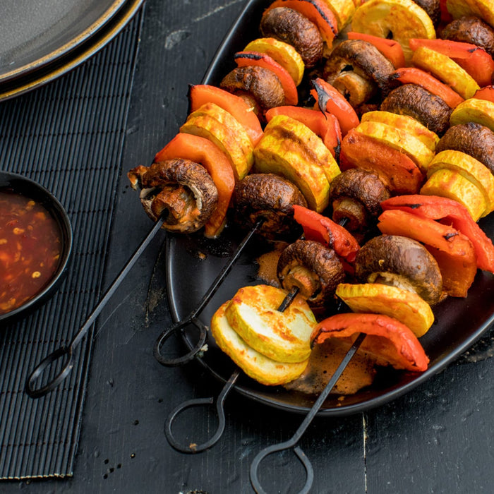 A plate of grilled vegetables and mushrooms on skewers.