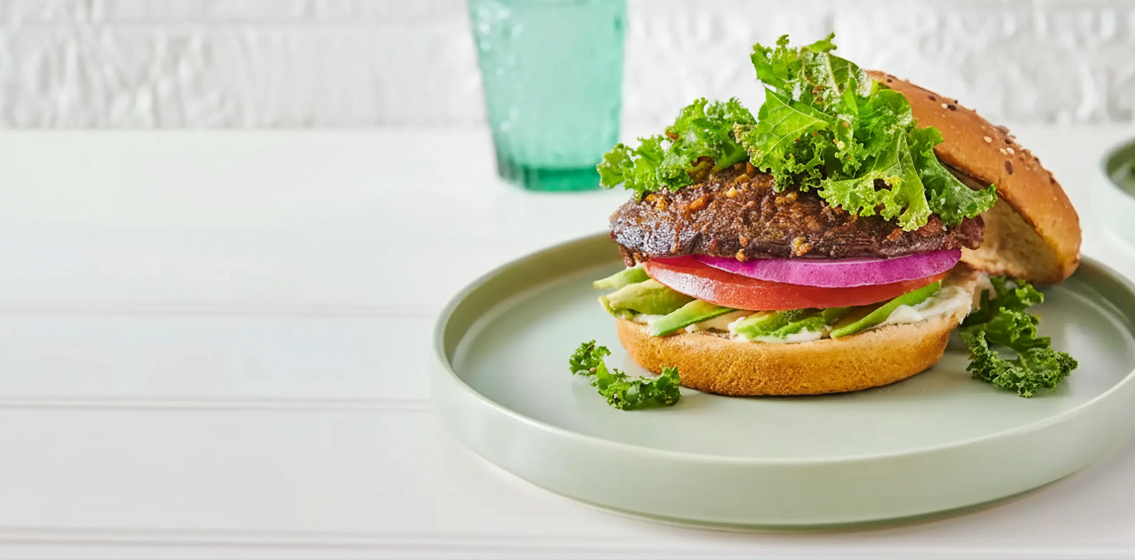Vegetarian burger with lettuce, tomato, and avocado on a green plate with a white background