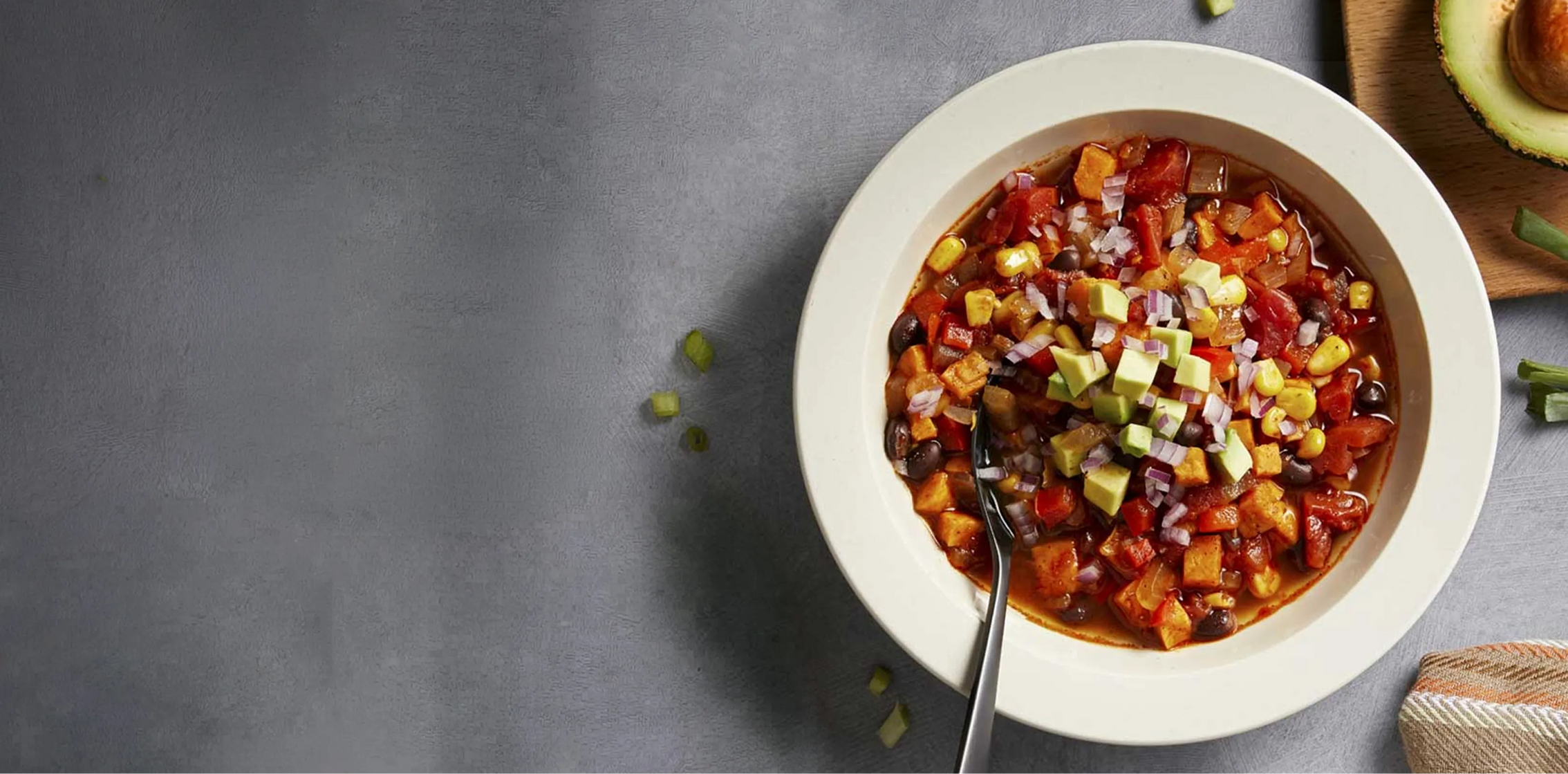 Bowl of chili with vegetables on a gray surface