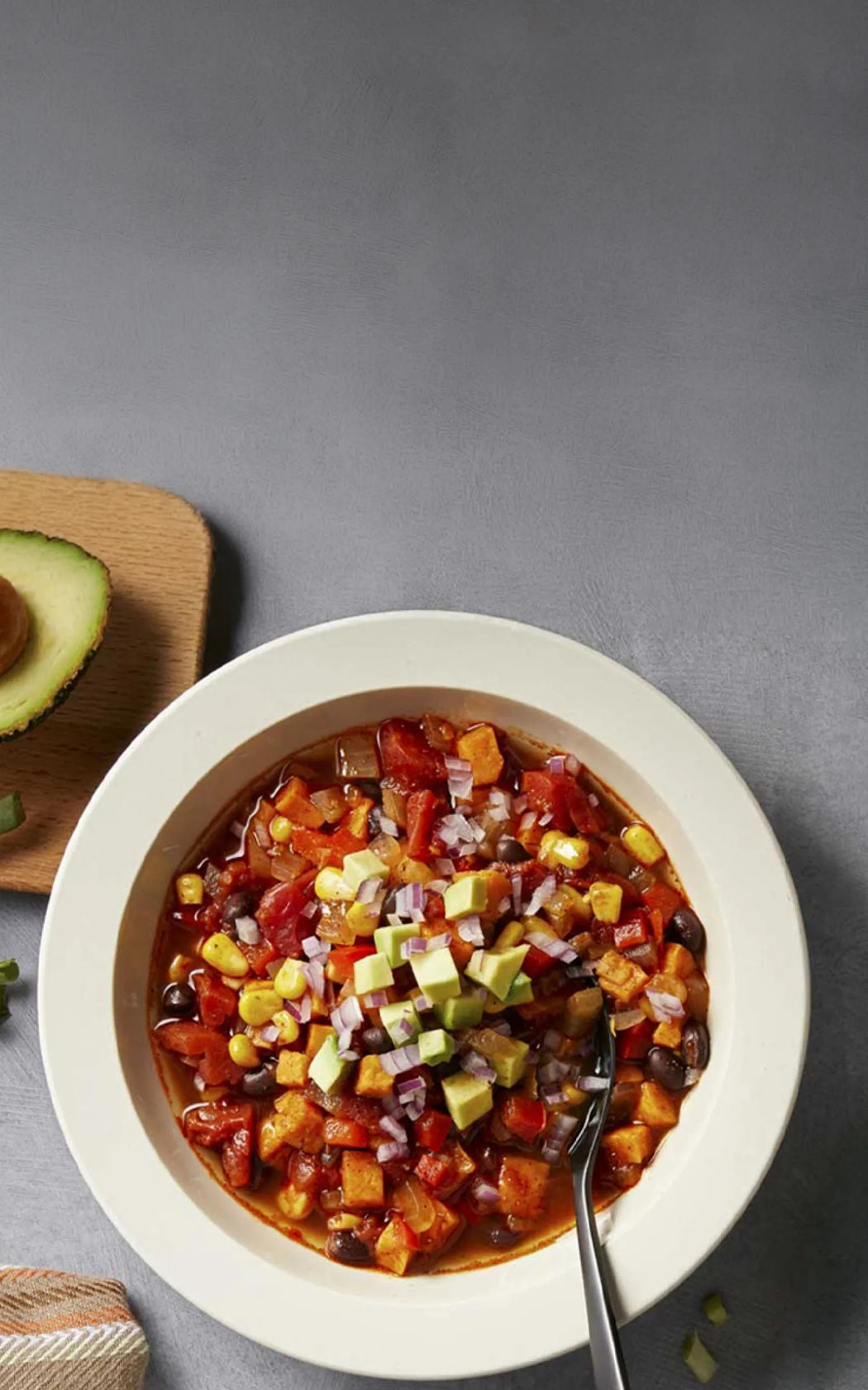 Bowl of chili with avocado and a spoon on a gray background