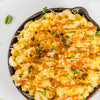 A close-up of a skillet of macaroni and cheese with a crispy, golden brown crust, topped with a drizzle of ketchup and fresh basil.
