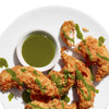 Fried chicken tenders are drizzled with a green sauce and served with a small bowl of the sauce.