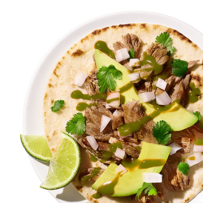 A close-up of a taco with meat, avocado, cilantro, and onions.