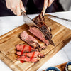 A person is carving a large piece of prime rib on a wooden cutting board.